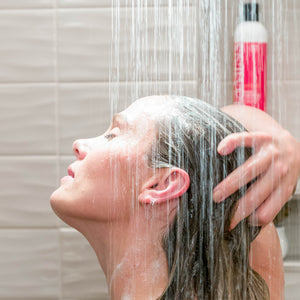 Woman showering with bottle of Vitamins Gold Label, Hair Growth Support Shampoo, with Biotin, Keratin, Saw Palmetto, Baicapil in the background