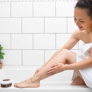Woman rubbing Organic Lavender Sugar Body Scrub with Coconut on her calf in the bathtub 