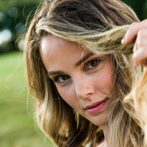 Close up view of woman peering into the camera lifting the front part of her hair as if she is playing peek a boo