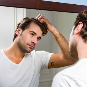 Man running fingers through his hair while gazing in the mirror