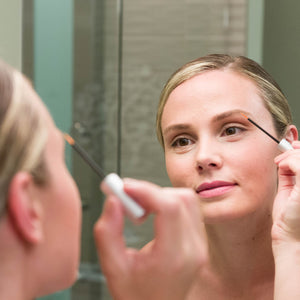 Woman applying Bang Brow Renewal Serum that includes Redensyl eyebrow serum to her eyebrow in the mirror